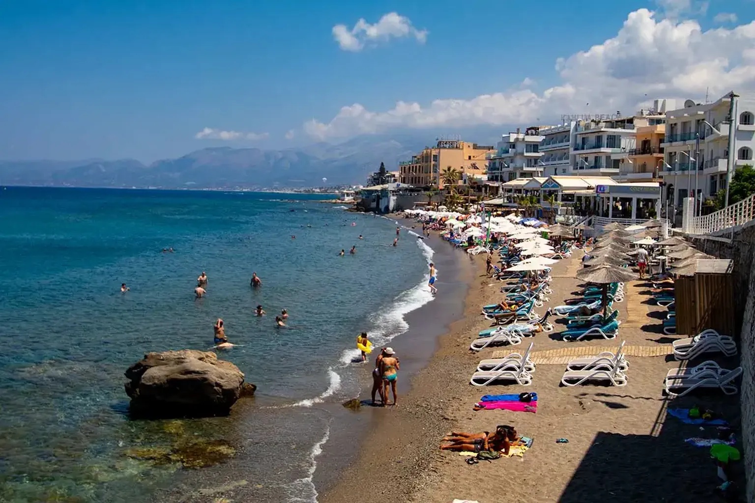 Παραλία στη Χερσόνησο Κρήτης με ξαπλώστρες, κρυστάλλινα νερά και επισκέπτες που απολαμβάνουν το μπάνιο τους κάτω από τον καλοκαιρινό ήλιο